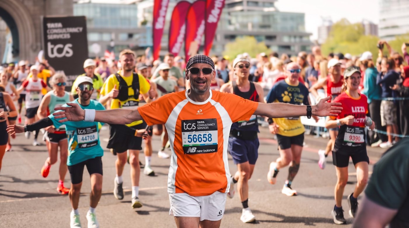Stephan Göckler läuft in orange-weißem Laufdress mit ausgebreiteten Armen und lachend über die Tower Bridge beim London-Marathon.